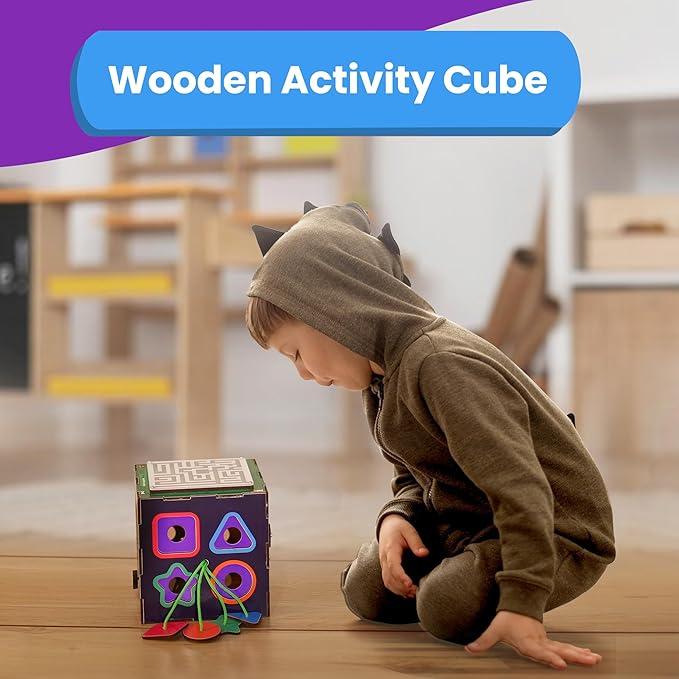Young child in a dinosaur hoodie curiously playing with a colorful wooden activity cube, featuring shape-sorting cutouts and a maze panel, with the “Wooden Activity Cube” displayed above.