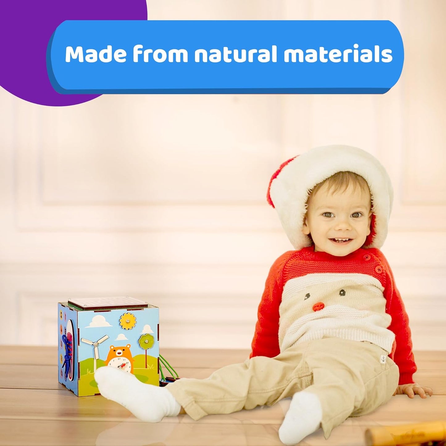 Smiling toddler wearing a festive outfit and sitting next to a colorful activity cube, with a banner above that reads “Made from natural materials,” highlighting the toy’s eco-friendly design.
